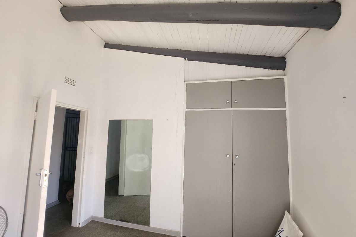 A bedroom featuring built-in cupboards, exposed ceiling beams, and a wall-mounted mirror, with access to an adjacent room.