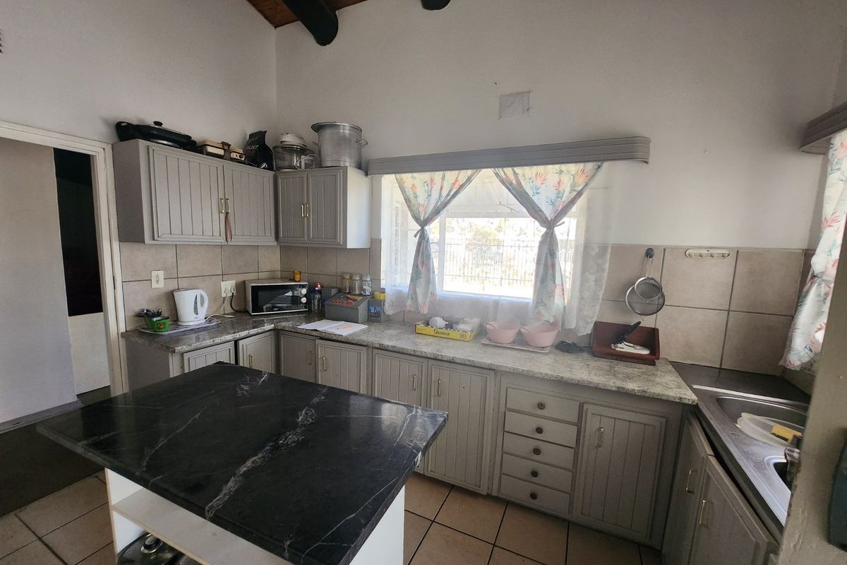 A functional kitchen featuring grey cabinetry, stone-look countertops, a central island with a dark stone top, and tiled flooring under a vaulted timber ceiling.