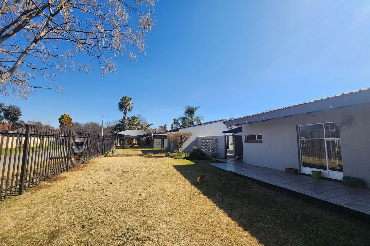 A spacious rear garden featuring a paved patio area, established lawn, and perimeter metal fencing, offering a private outdoor space.