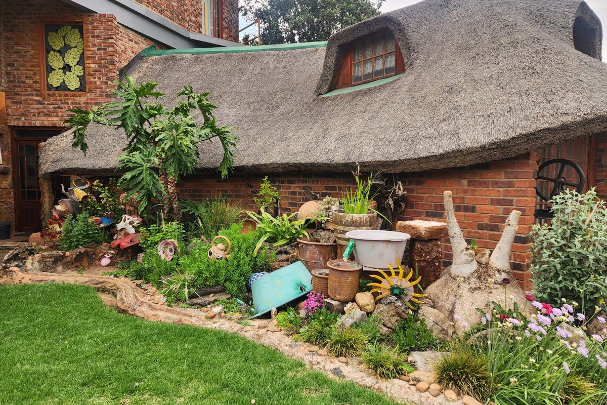 A view of the rear garden featuring a traditional thatched roof structure with exposed brick walls and a small dormer window.