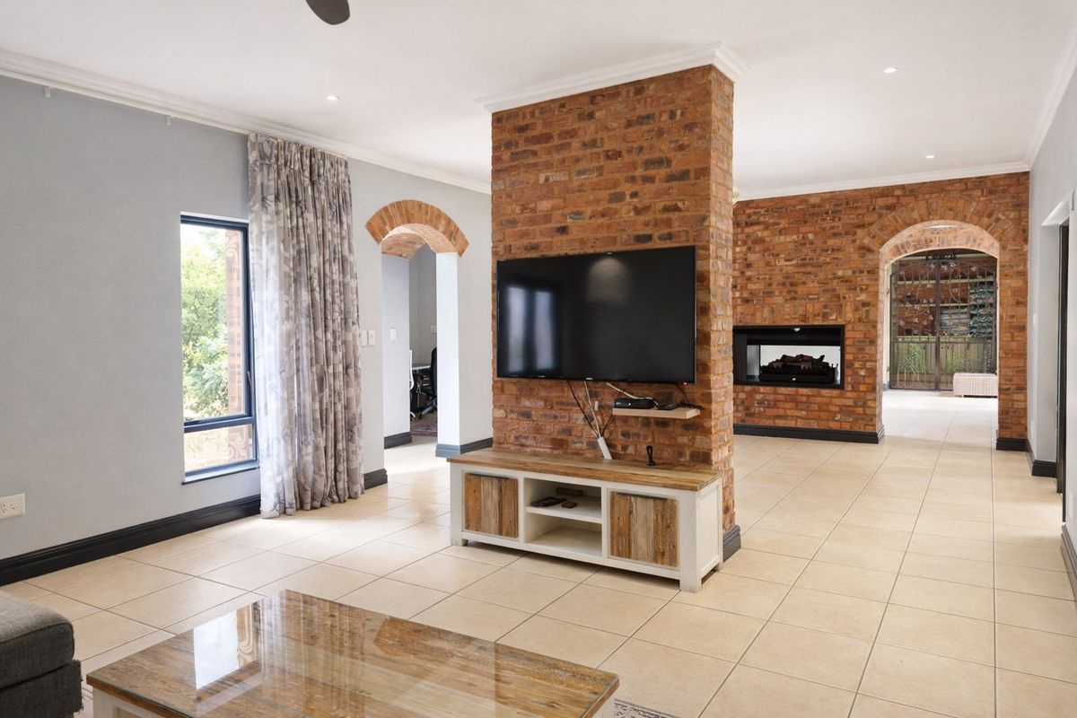 Spacious living area featuring a prominent exposed brick wall with a built-in fireplace, tiled flooring, and elegant archways connecting to adjacent rooms.
