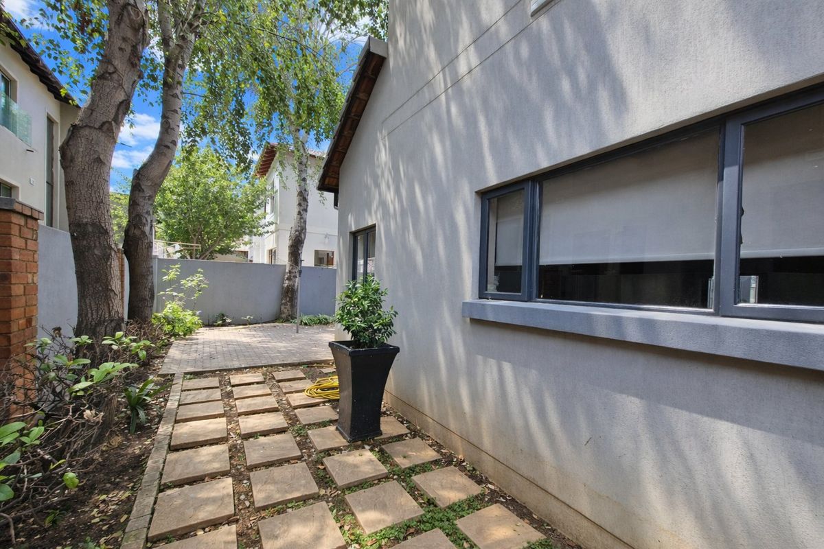 A side garden area featuring a paved walkway, a small patio space, and a boundary wall, providing a private outdoor retreat.