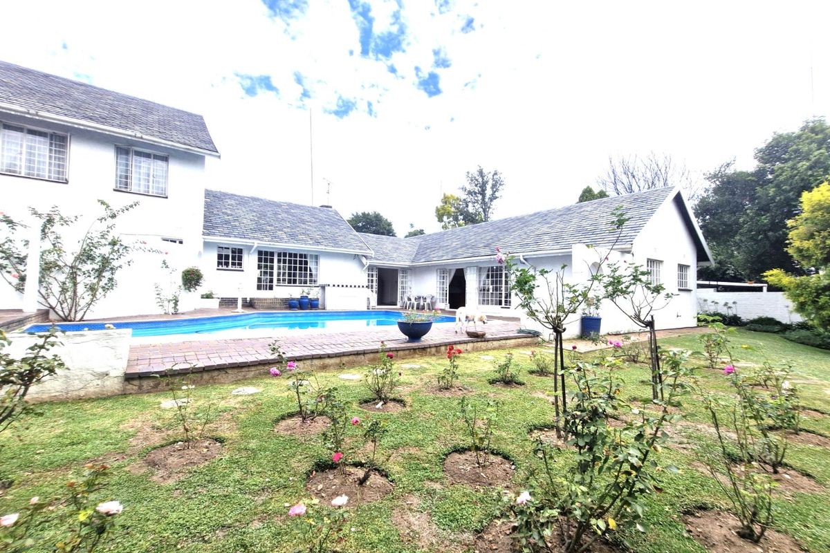Rear view of the house featuring a swimming pool, brick paved patio area, and a well-maintained garden with established rose bushes.
