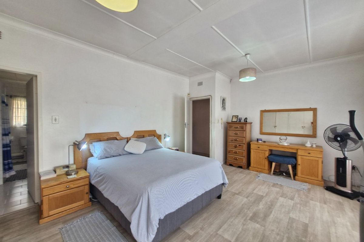 A spacious bedroom featuring light-toned laminate flooring, neutral walls, and a classic ceiling design with integrated lighting fixtures.