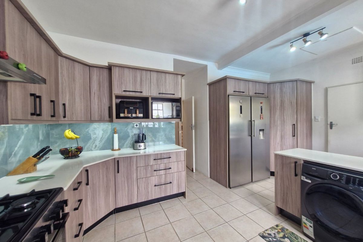 Modern kitchen featuring wood-grain cabinetry, stone countertops, gas hob, extractor fan, and integrated appliances including a washing machine and double-door fridge.