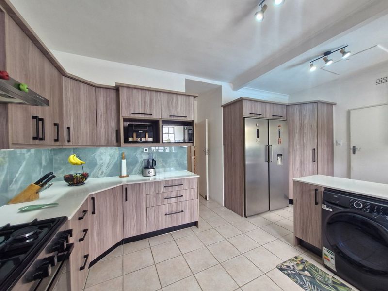 Modern kitchen featuring wood-grain cabinetry, stone countertops, gas hob, extractor fan, and integrated appliances including a washing machine and double-door fridge.
