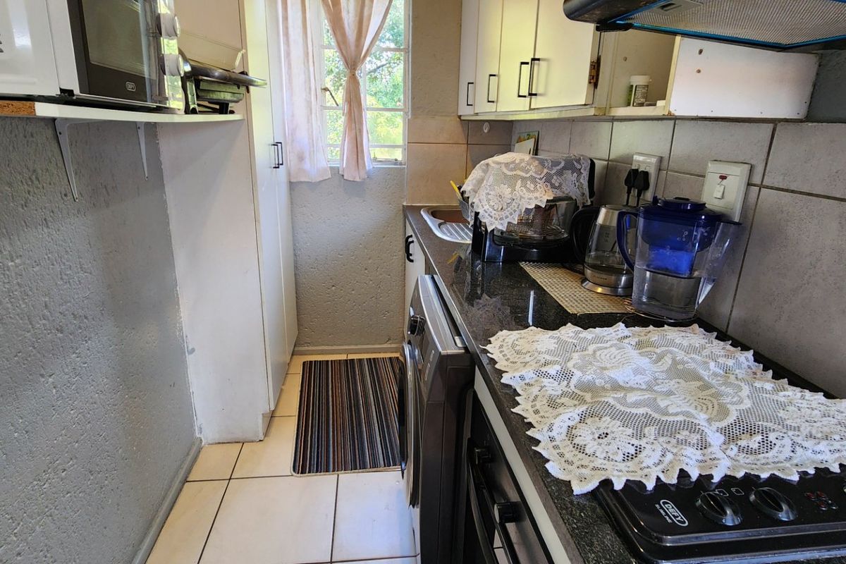 Compact kitchen featuring granite countertops, built-in oven, hob, extractor fan, and tiled finishes, offering a functional layout for efficient meal preparation.