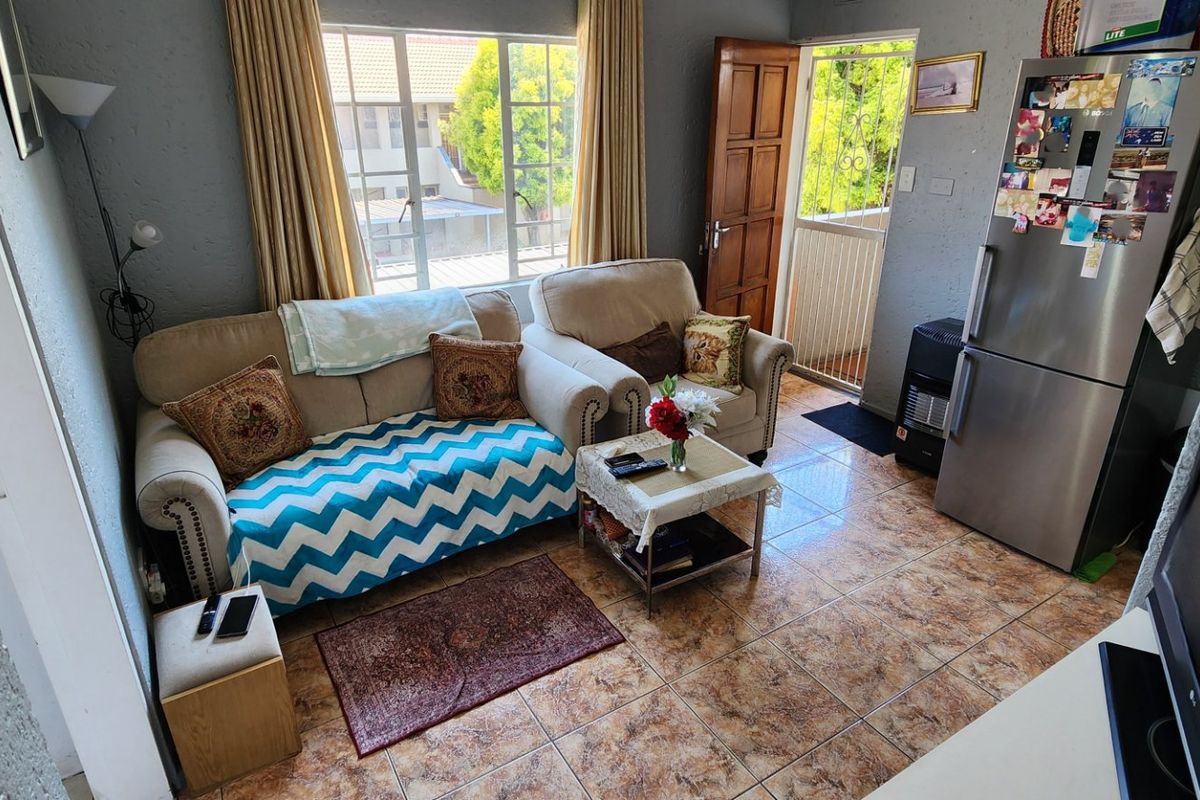 A compact living area featuring tiled flooring, natural light from the window, and direct access to an exterior entrance with a security gate.