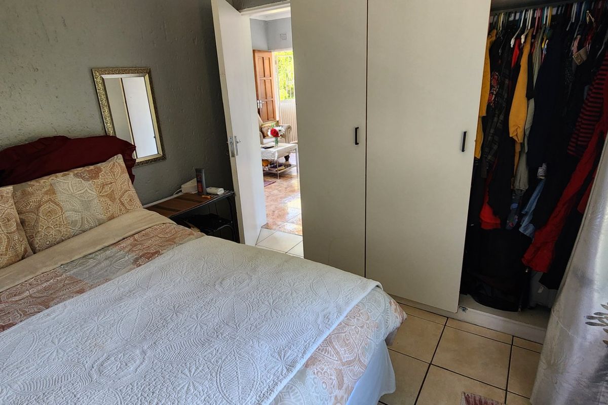 A bedroom featuring tiled flooring and a built-in wardrobe, with a view through the doorway into an adjacent living space.