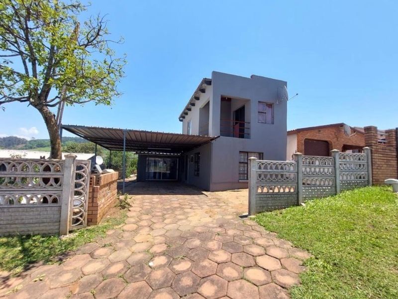 Front view of a two-story house featuring a paved driveway, attached carport, and a precast concrete boundary wall.