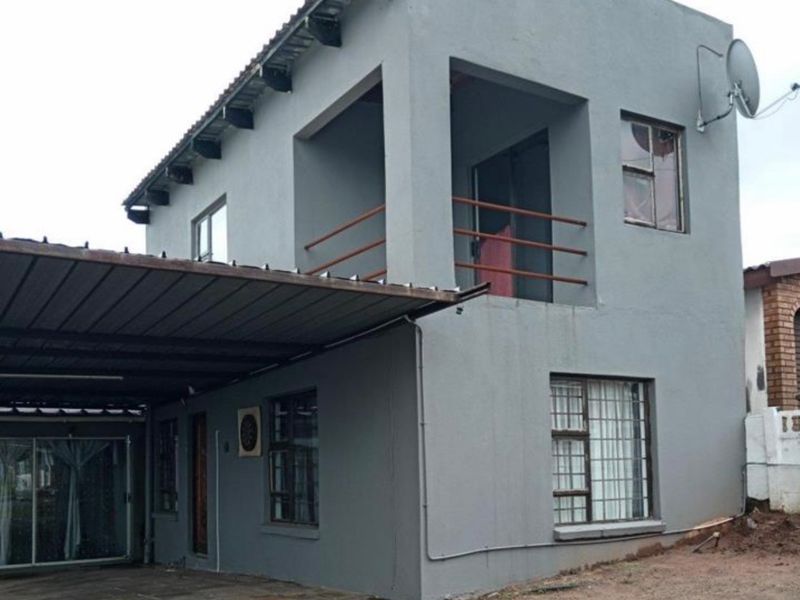 Two-story residential property featuring a carport, upper-level balcony with metal railings, and a paved driveway area.