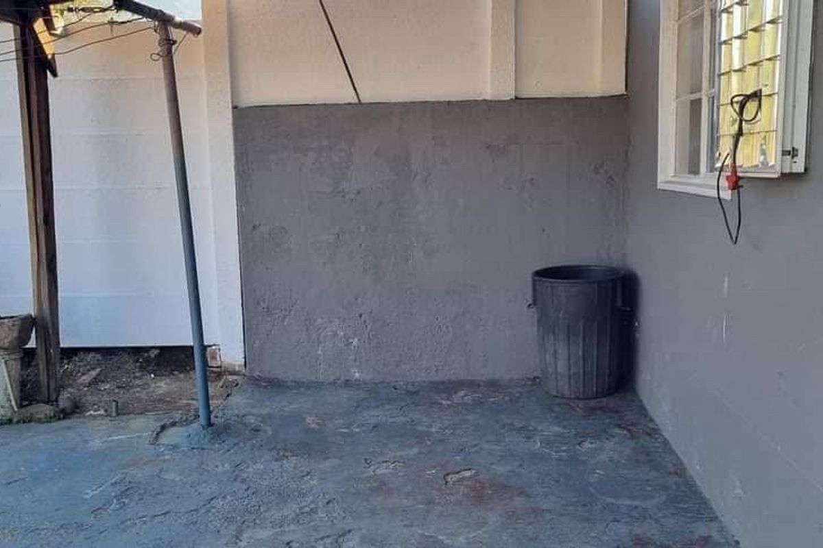 A rear exterior patio area featuring a concrete floor, precast boundary wall, and louvered window, showing signs of wear and requiring maintenance.