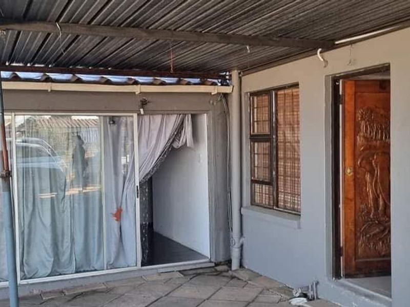 A covered outdoor patio area featuring tiled flooring, a sliding glass door, and a decorative carved wooden entrance door.