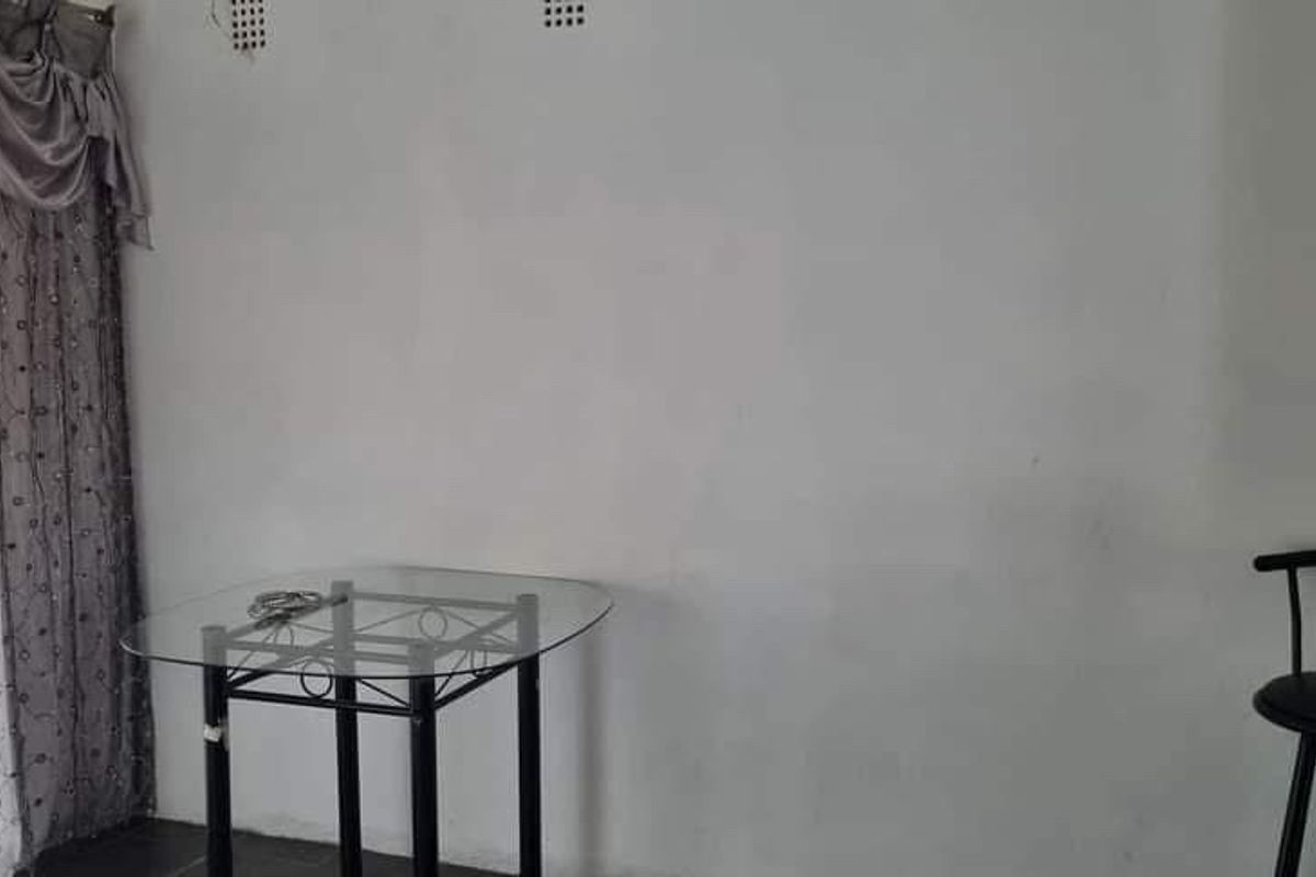 A living area featuring tiled flooring and curtain rails, currently showing signs of wear on the wall surfaces.