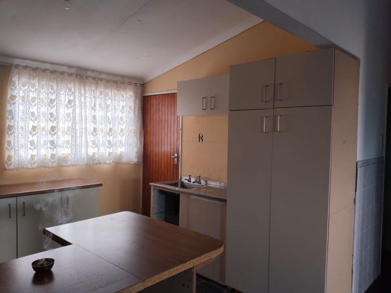 A dated kitchen area featuring built-in cabinetry, a stainless steel sink, and laminate countertops, requiring cosmetic updates to modernize the space.