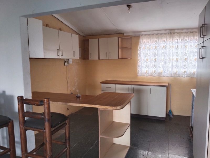 A functional kitchen featuring built-in cabinetry, laminate countertops, and a breakfast bar, offering a practical layout with potential for cosmetic updates.