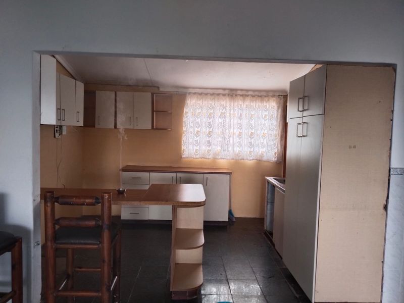 A dated kitchen featuring built-in cabinetry, a breakfast bar, and tiled flooring, offering potential for a modern renovation.