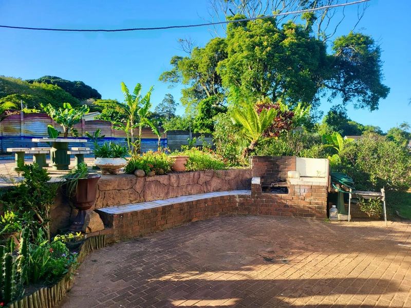 Outdoor patio area featuring a built-in brick braai, paved flooring, and a curved retaining wall with integrated seating, set within a landscaped garden.