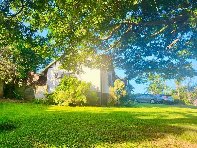 A view of the rear garden and side elevation of the house, featuring a well-maintained lawn and mature trees.
