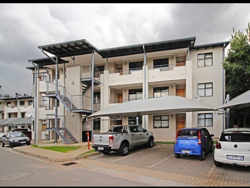Exterior view of a multi-story apartment complex featuring paved parking, shade cloth carports, and external metal staircases.