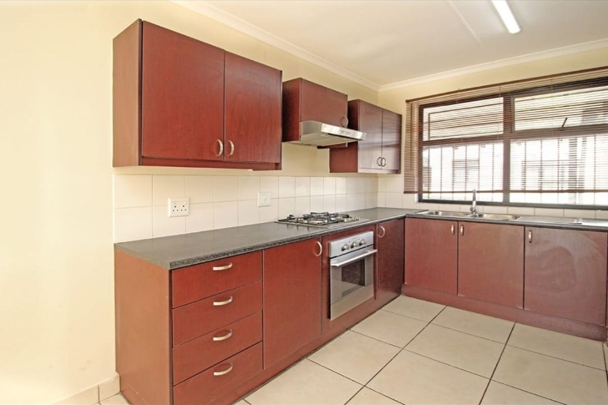 A functional kitchen featuring dark wood cabinetry, laminate countertops, a gas hob, built-in oven, and tiled flooring with a large window for natural light.