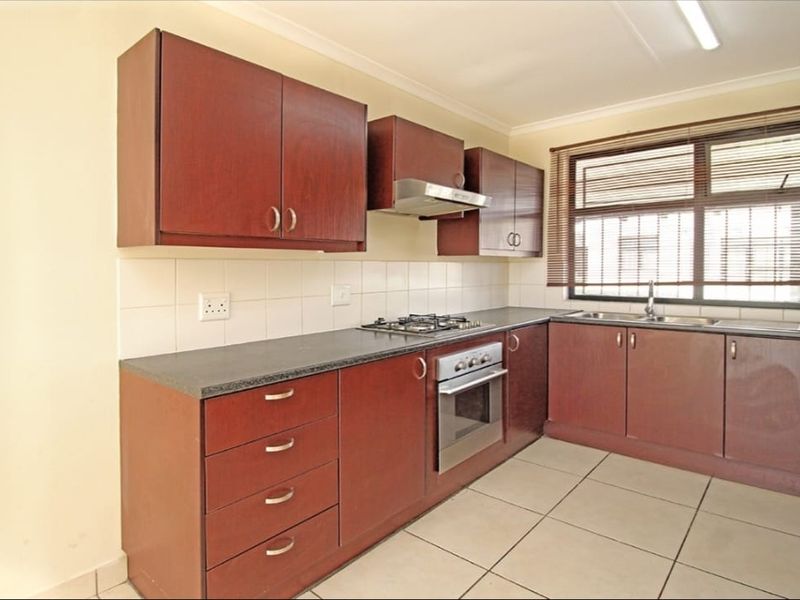 A functional kitchen featuring dark wood cabinetry, laminate countertops, a gas hob, built-in oven, and tiled flooring with a large window for natural light.