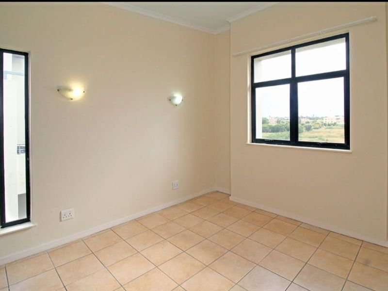 A bright, empty bedroom featuring neutral tiled flooring, black-framed windows, and wall-mounted lighting, offering a clean canvas for personalization.