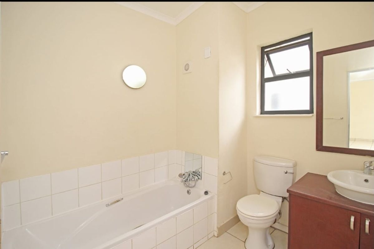 A functional bathroom featuring a bathtub, toilet, and vanity basin with tiled splashbacks and natural light from a window.