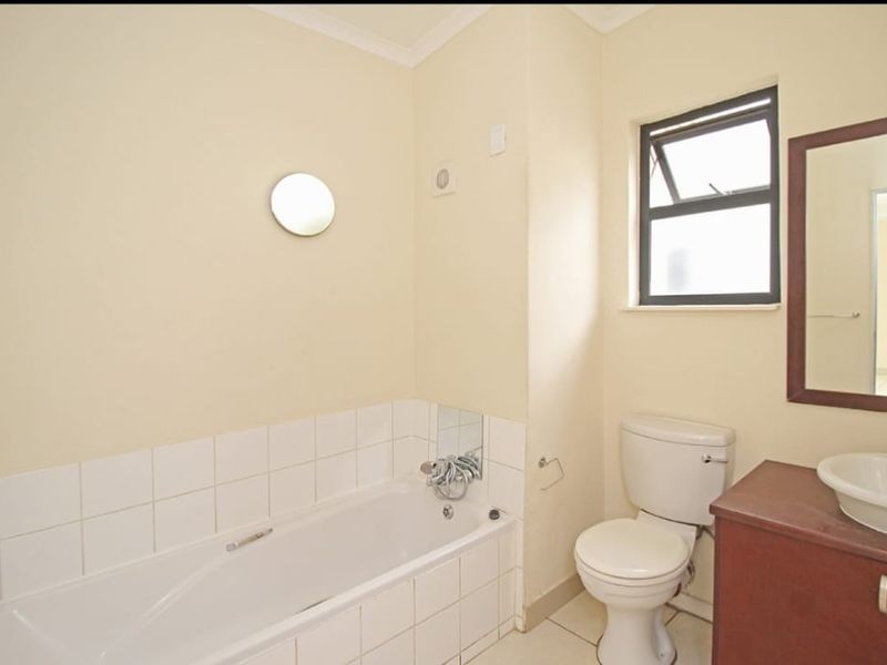 A functional bathroom featuring a bathtub, toilet, and vanity basin with tiled splashbacks and natural light from a window.