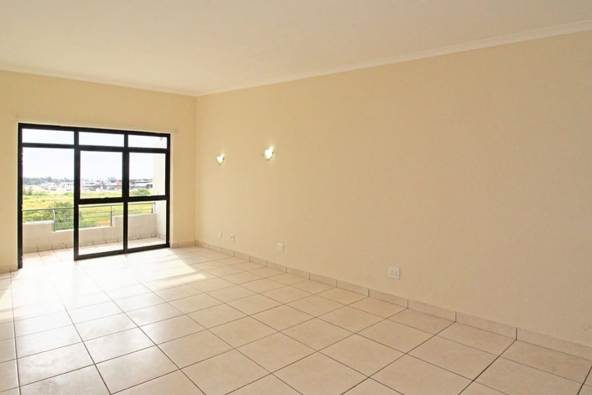 A bright, empty living room featuring neutral tiled flooring and a large sliding glass door providing access to an outdoor balcony area.