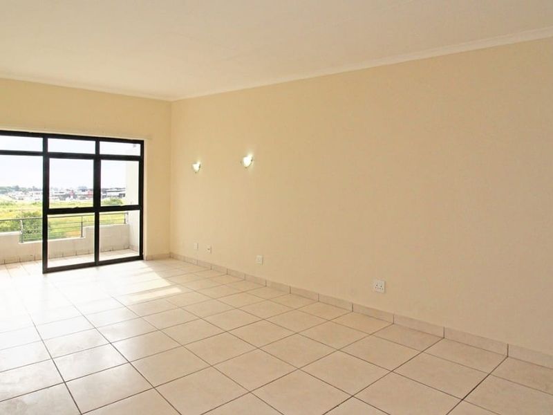 A bright, empty living room featuring neutral tiled flooring and a large sliding glass door providing access to an outdoor balcony area.