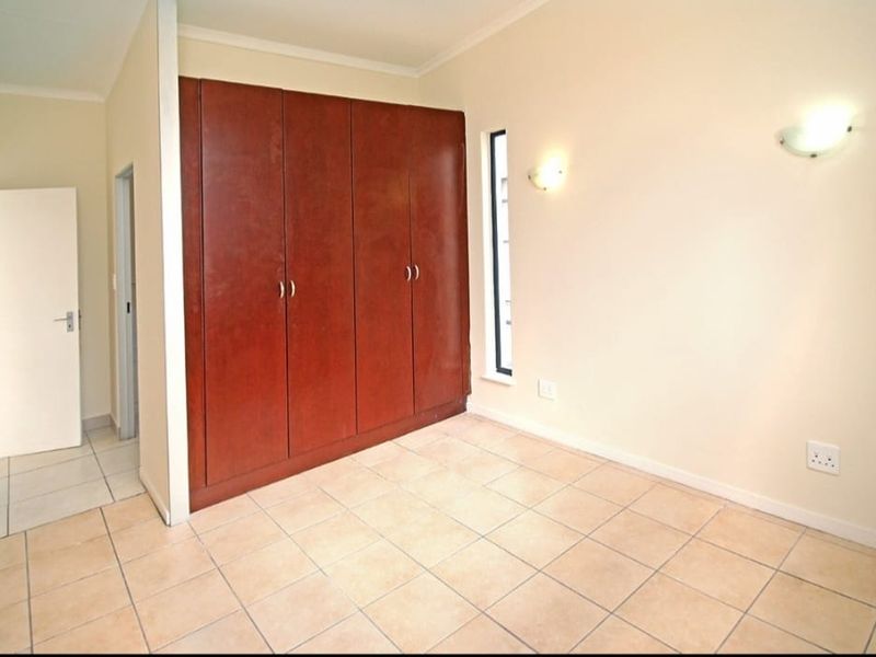 A clean, empty bedroom featuring tiled flooring, built-in wooden cupboards, and wall-mounted lighting fixtures.