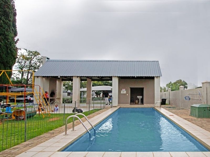 Communal pool area featuring a rectangular swimming pool, paved surround, and a covered patio structure with a built-in braai facility.
