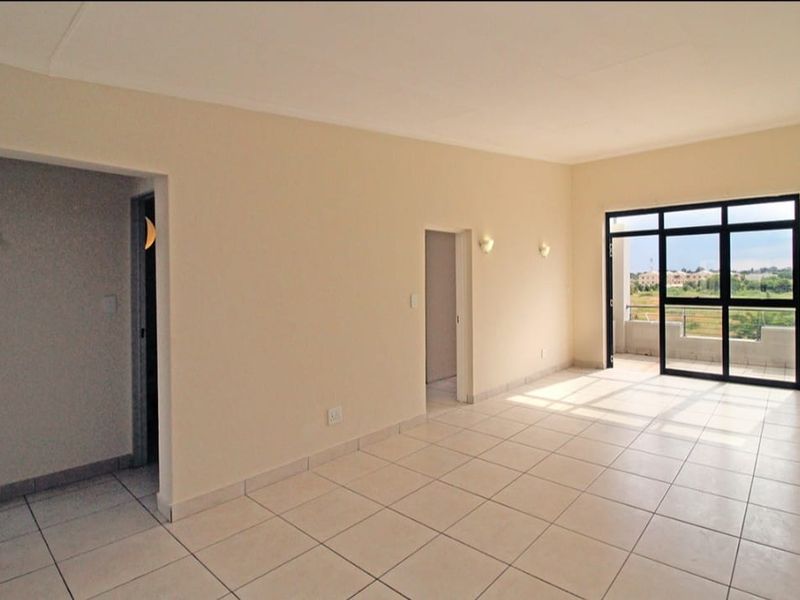 A bright, empty living area featuring neutral tiled flooring and a large sliding glass door leading to an outdoor balcony.