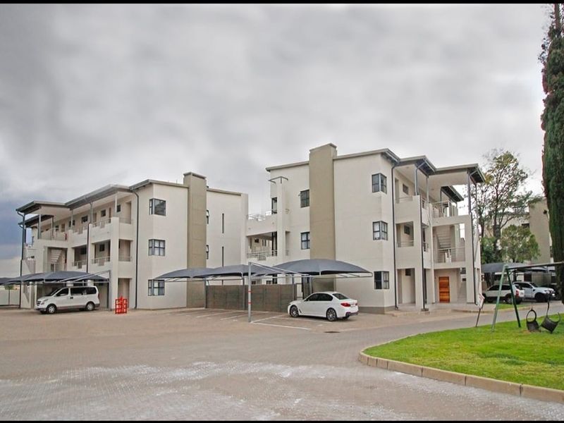 Exterior view of modern multi-story apartment buildings featuring paved parking areas with shade cloth carports and landscaped grounds.