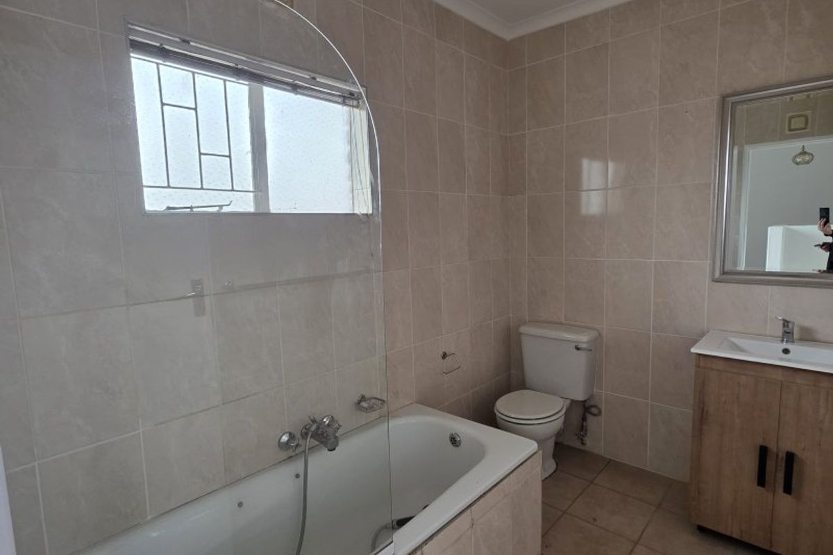 A functional bathroom featuring a built-in bathtub with a glass screen, a vanity cabinet with a basin, and neutral wall and floor tiling.