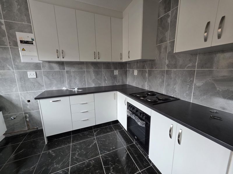Modern kitchen featuring white cabinetry, dark countertops, tiled backsplash, and built-in oven and hob. The space is currently vacant and ready for final finishing.