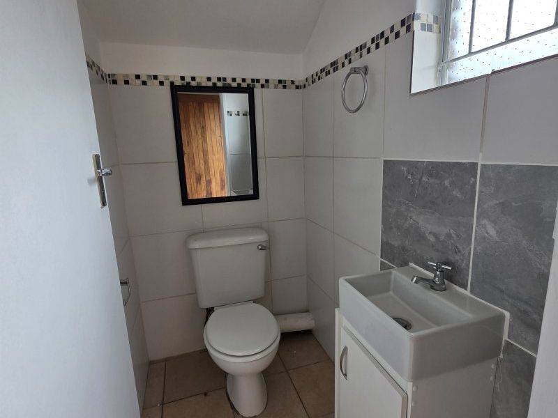 A compact bathroom featuring a toilet, vanity basin, tiled finishes, and a security window grille.
