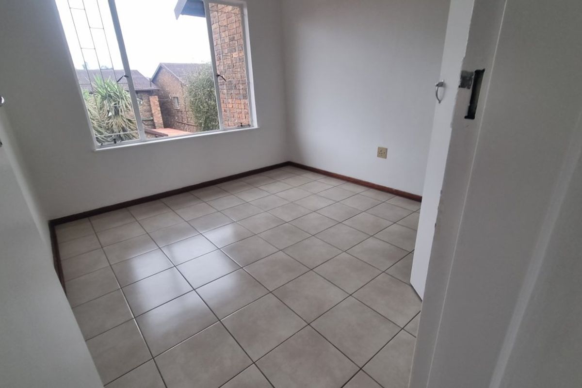An empty bedroom featuring neutral tiled flooring, a window with security bars, and standard finishes, ready for personalization.