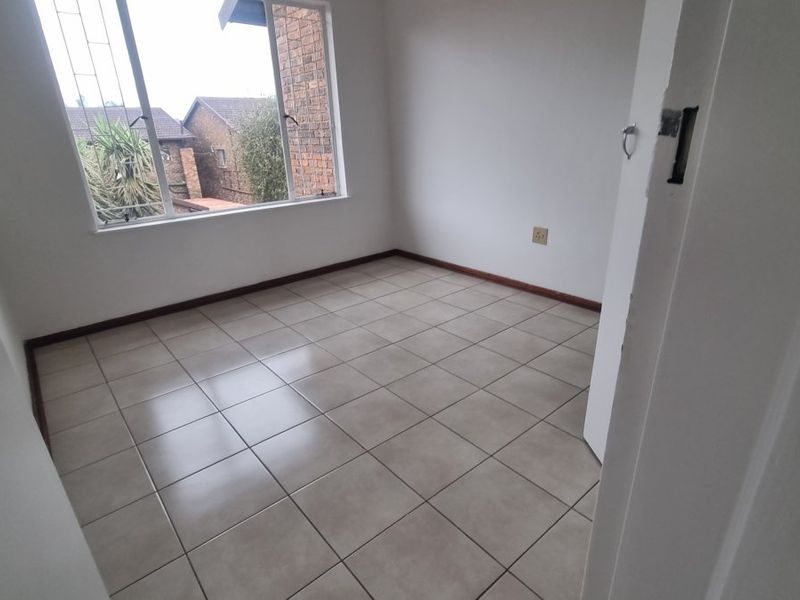 An empty bedroom featuring neutral tiled flooring, a window with security bars, and standard finishes, ready for personalization.