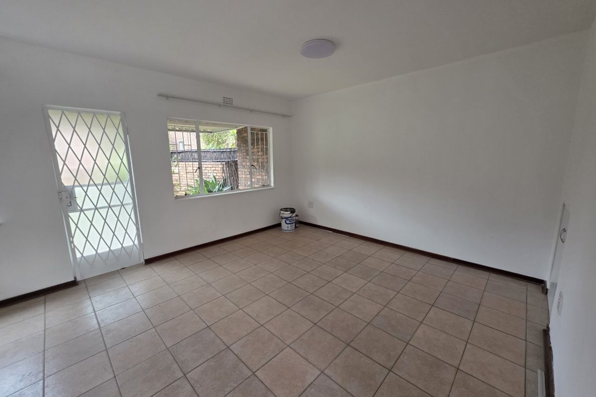 An empty, neutrally painted living area featuring tiled flooring, a security gate, and a window with security bars.