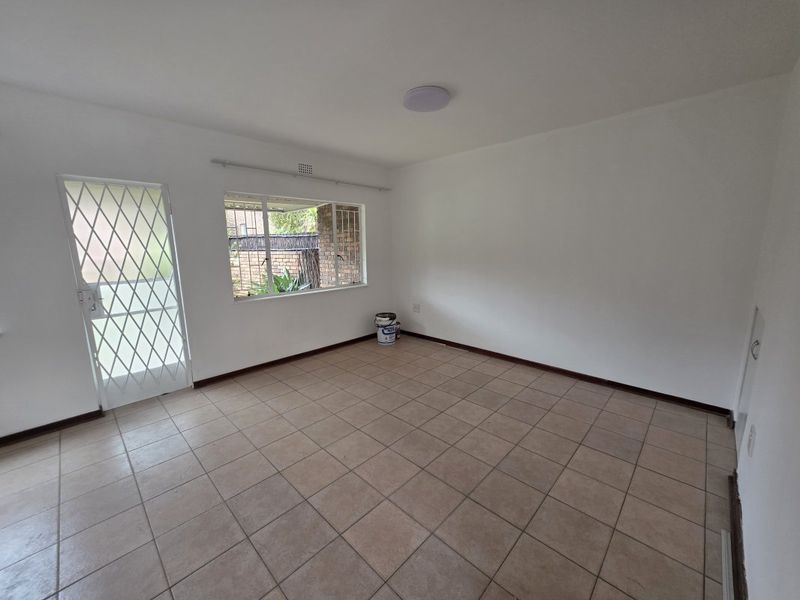 An empty, neutrally painted living area featuring tiled flooring, a security gate, and a window with security bars.