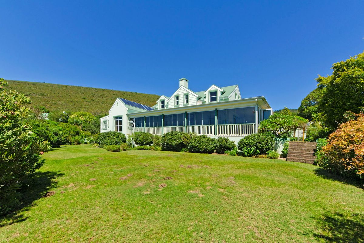 A view of the rear exterior of the house, featuring a large lawn, landscaped garden, and a covered patio with glass enclosures.