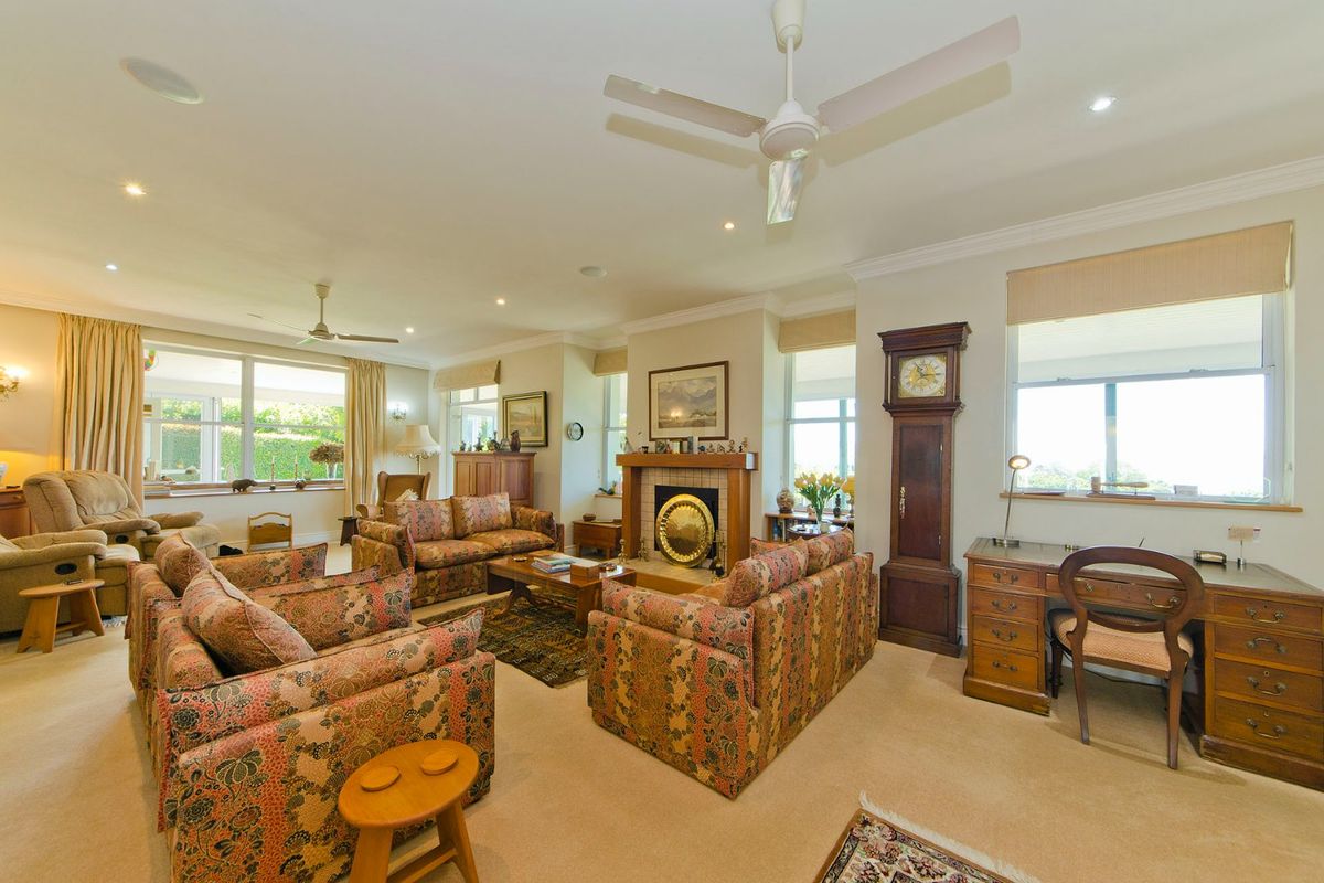 Spacious living room featuring a central fireplace with a timber mantel, recessed downlighting, and ceiling fans, offering a comfortable and traditional living space.