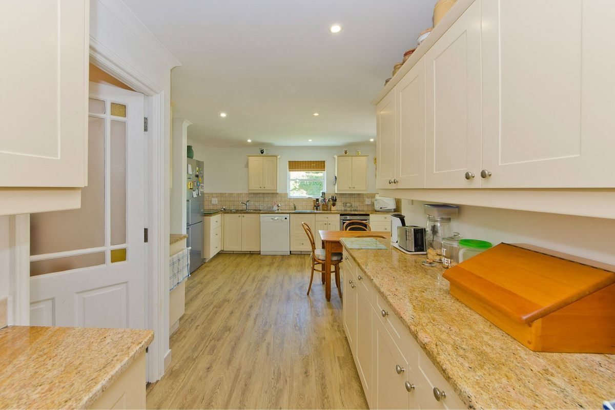 A functional kitchen featuring light-toned cabinetry, granite countertops, tiled backsplash, and wood-look flooring, offering a practical layout with ample storage space.