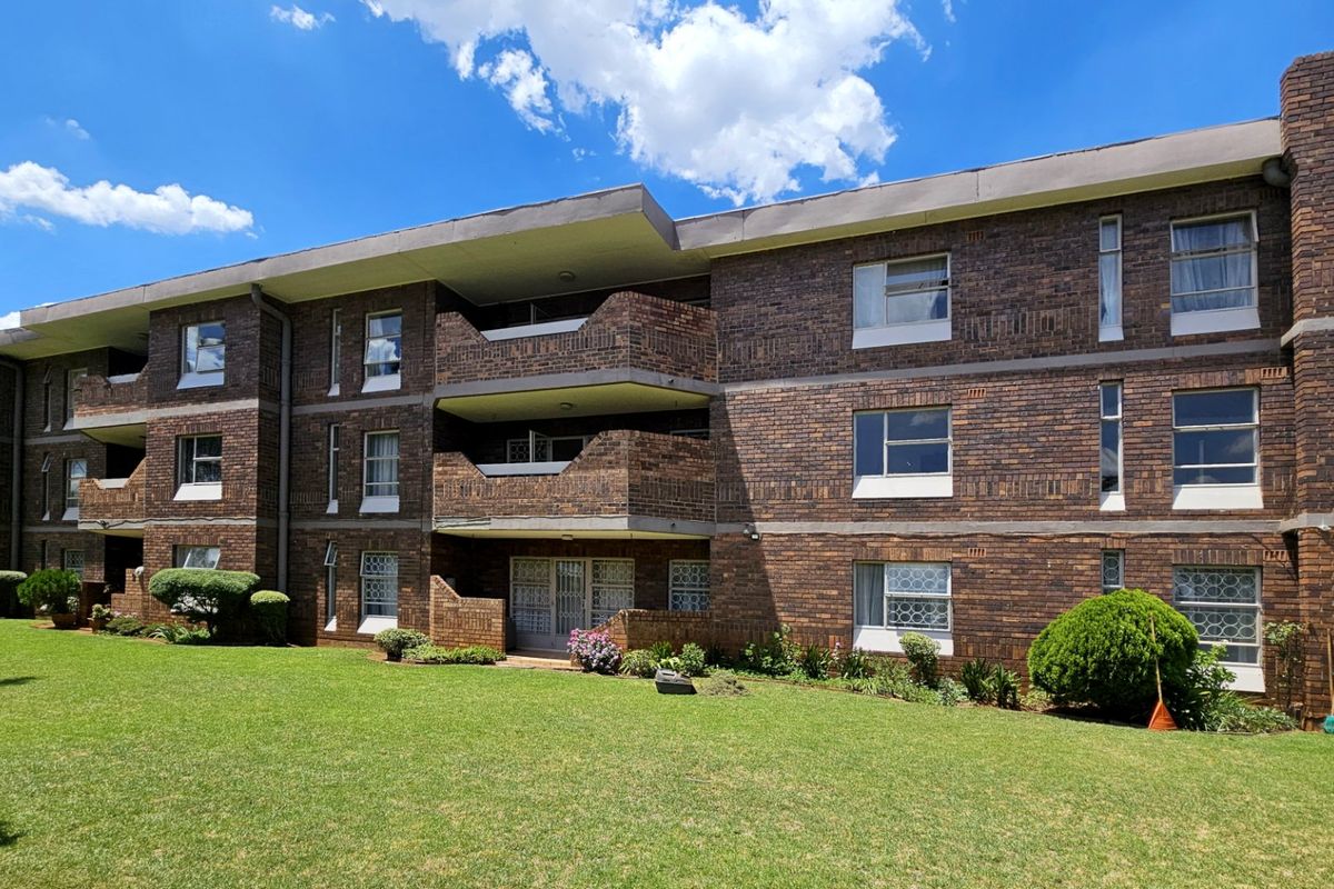 A multi-story apartment building featuring a classic face brick facade, private balconies, and well-maintained surrounding lawn areas.