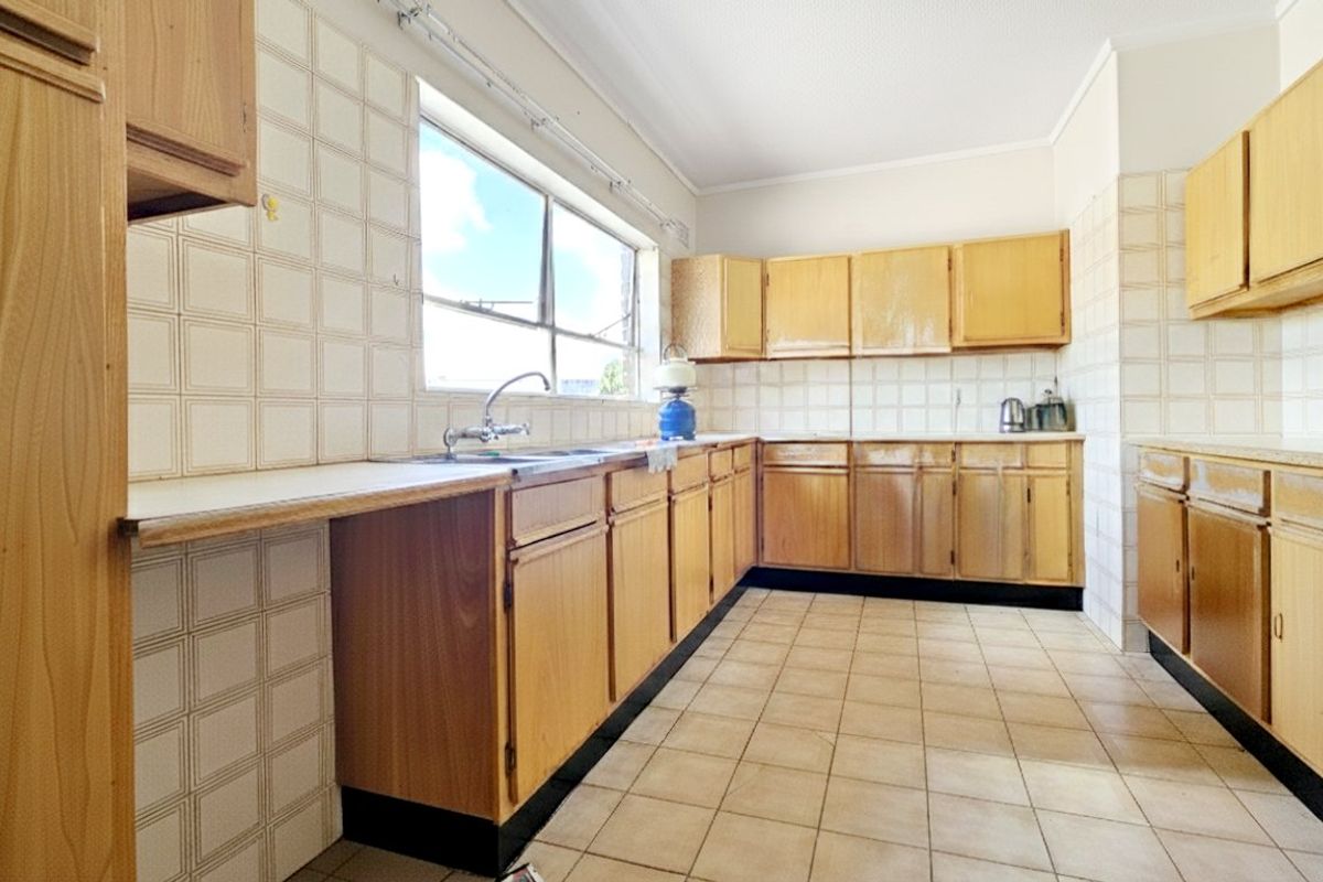 A functional kitchen featuring original timber-look cabinetry, tiled splashbacks, and ceramic floor tiles, offering a blank canvas for modern renovation.
