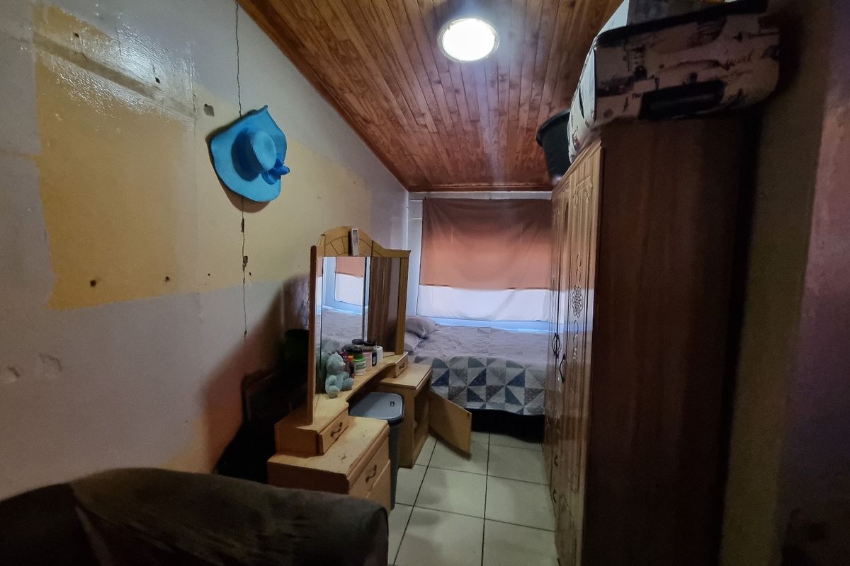 A bedroom featuring a timber-clad ceiling, tiled flooring, and visible wall surface damage requiring repair and cosmetic updates.