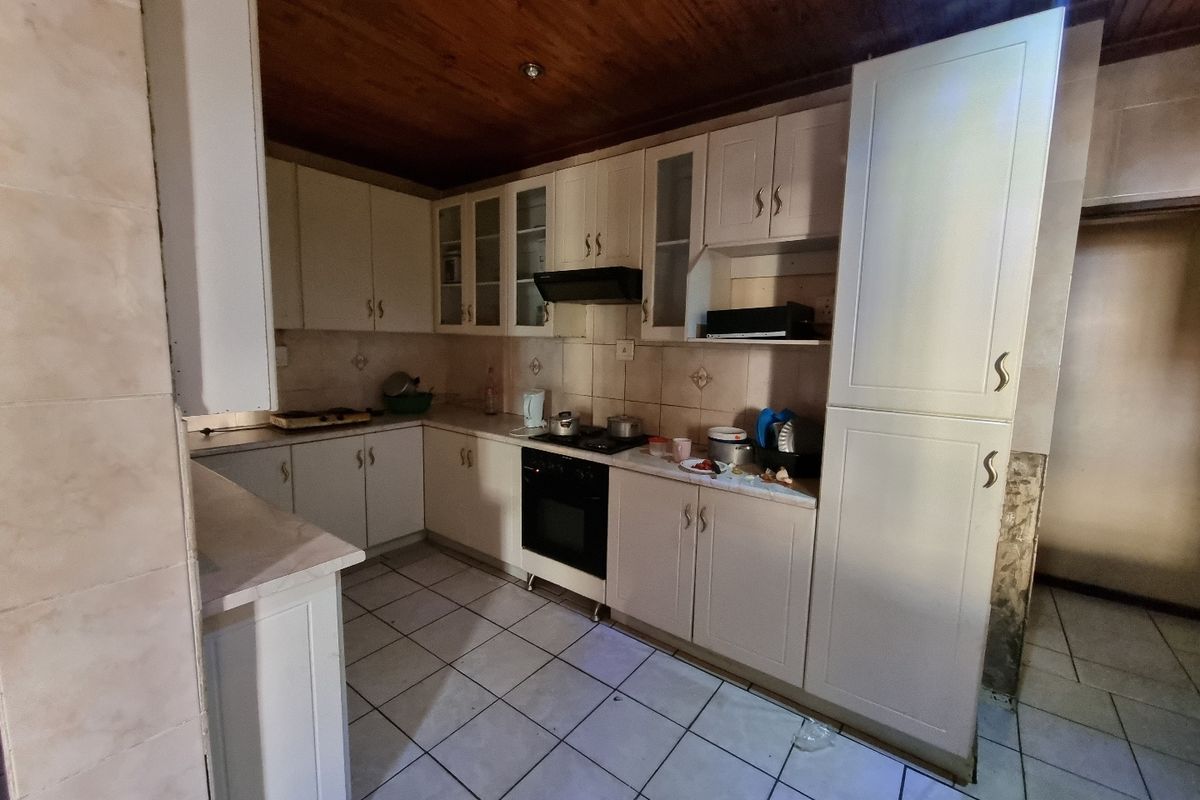 A dated kitchen featuring white cabinetry, tiled flooring, and a wood-paneled ceiling, equipped with a built-in oven and hob.