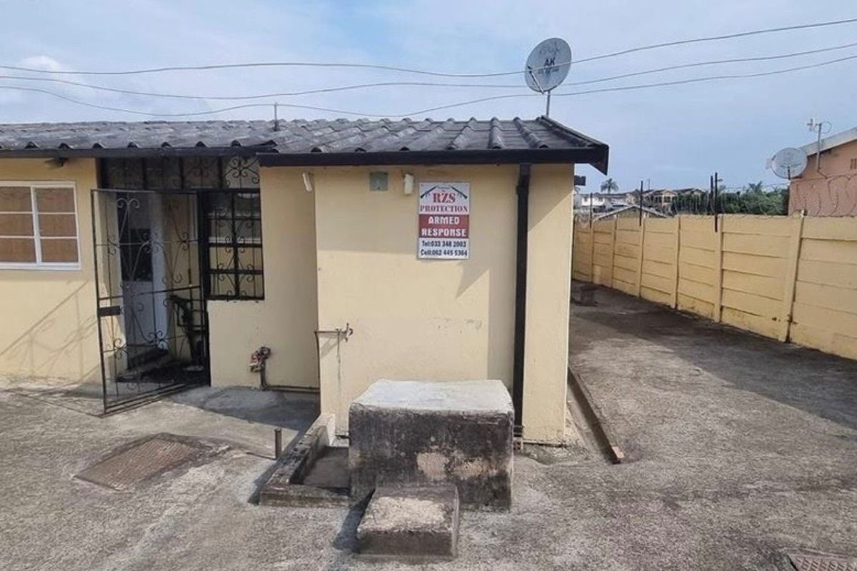Rear exterior view of the property featuring a concrete paved yard, boundary wall with security spikes, and a security gate.